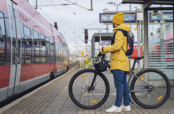 Mensch steht mit Fahrrad am Bahnsteig.