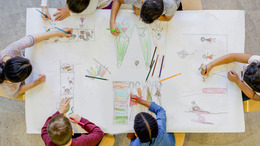 Eine Gruppe Kinder sitzt am Tisch und malt gemeinsam ein Bild