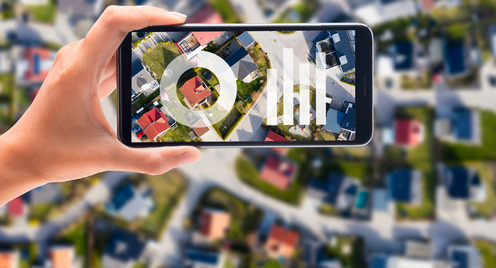 Eine Hand hält ein Smartphone, im Hintergrund ist eine Stadtsilhouette. Auf dem Display sind Balkendiagramme zu sehen.