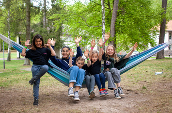 Fünf Kinder und Jugendliche sitzen gemeinsam in einer Hängematte, haben die Hände in die Höhe gereckt und lächeln in die Kamera.