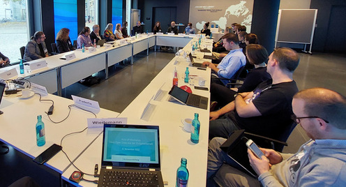 [Translate to English:] Workshop-Raum im Berliner Gebäude der Bertelsmann Stiftung. Eine Tischgruppe im Rechteck um die sich rund 30 Personen sitzend versammeln.