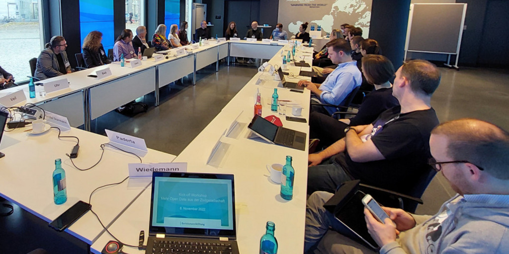 Workshop-Raum im Berliner Gebäude der Bertelsmann Stiftung. Eine Tischgruppe im Rechteck um die sich rund 30 Personen sitzend versammeln.