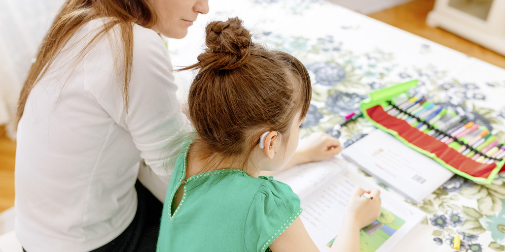 Mutter hilft ihrer Tochter, die Hörgeräte trägt, bei den Schulaufgaben