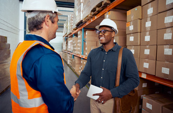 Zwei Arbeiter begrüßen sich. Sie ragen beiden einen Arbeitshelm.