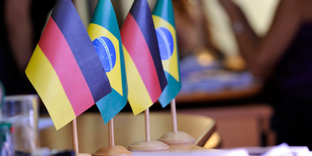 Small flags in the colors of Germany and Brazil stand on a table. In the background one can vaguely recognize people sitting around another table.