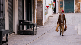 An old man with a medical mask goes with his few purchases through a deserted street of Tunis