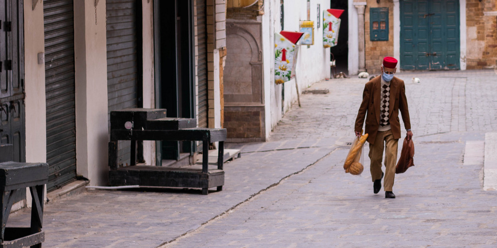 Ein alter Mann mit medizinischer Maske geht mit seinen wenigen Einkäufen durch eine menschenleere Straße von Tunis