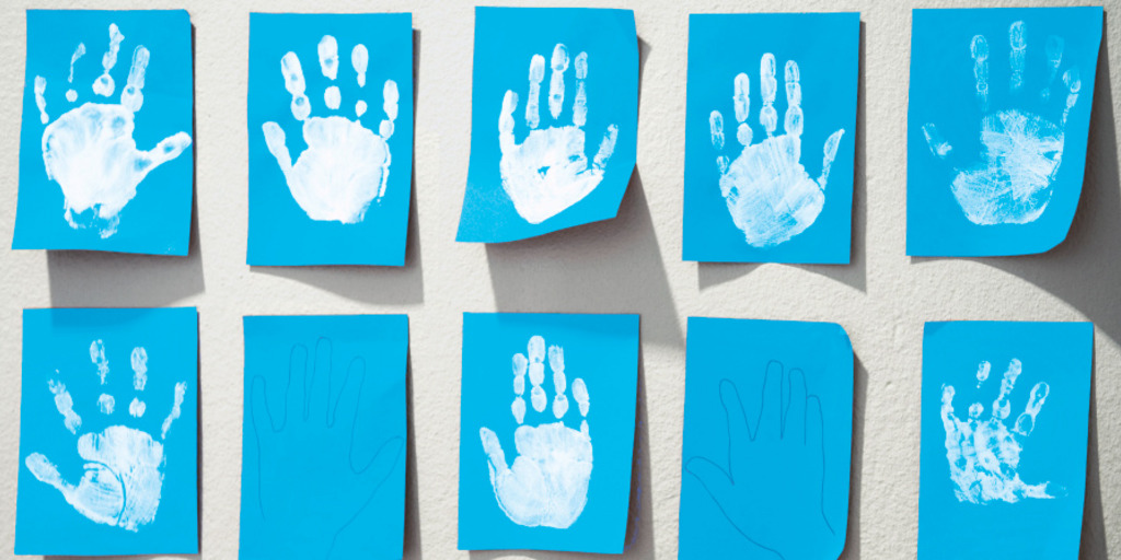Weiße Abdrücke von Kinderhänden auf blauen Zetteln hängen in mehreren Reihen an der Wand einer Kindertagesstätte.
