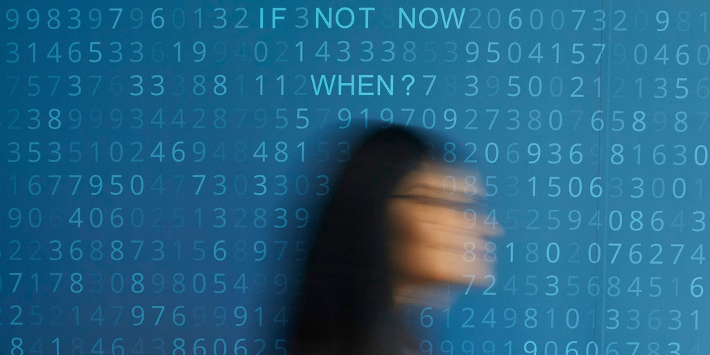 Bewegungsunschärfe einer Frau vor dem blauen Hintergrund und Zahlencode, auf dem der Schriftzug "IF NOT NOW WHEN" erkennbar ist.