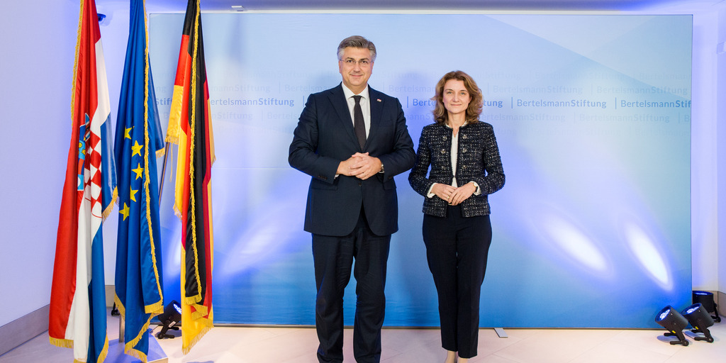 Der kroatische Premierminister Andrej Plenković posiert mit Daniela Schwarzer, Vorständin der Bertelsmann Stiftung, im Berliner Gebäude der Stiftung vor einer angestrahlten Wand und neben den Flaggen Kroatiens, Deutschlands und der EU für ein Foto.