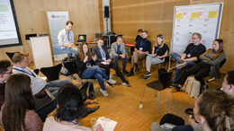 Gut zwei Dutzend Personen sitzen in einem Stuhlkreis und diskutieren. Im hintergrund ist das Open-Data-Barcamp-Logo zu sehen.