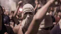 A protester at an anti-government rally in the Lebanese capital of Beirut is wearing his t-shirt as a mask in order to protect himself against tear gas. Next to and behind him, other protesters have raised their arms.