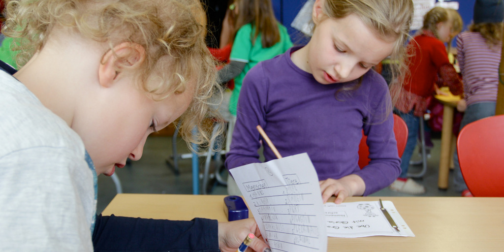 Zwei Kinder sitzen an einem Tisch und machen Schulaufgaben.