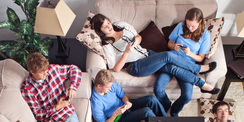 Jugendliche sitzen mit dem Handy beschäftigt auf der Couch
