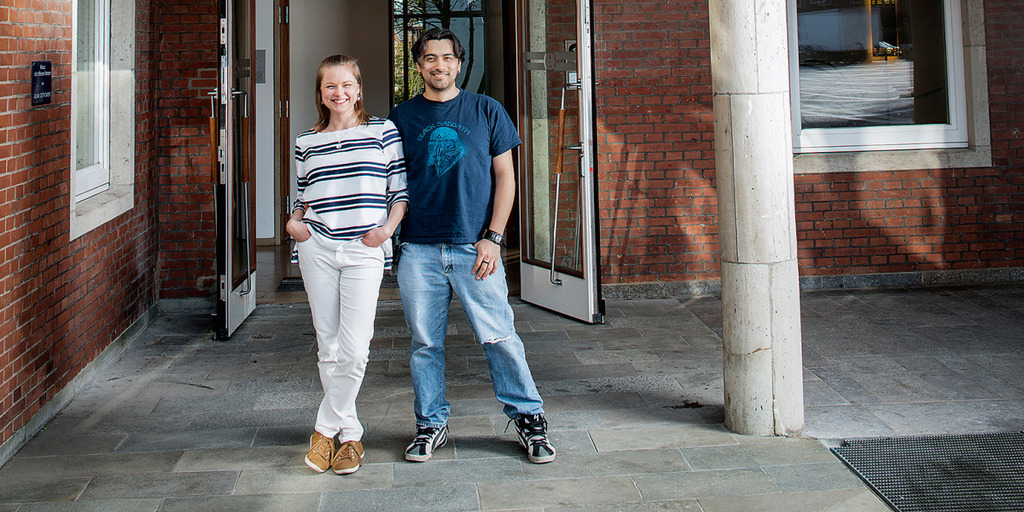 Eine junge Frau und ein junger Mann stehen vor der Eingangstür eines Backsteinhauses.