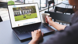 Eine Person sitzt am Tisch mit einer Tasse Kaffee und einem Laptop. Auf dem Bildschirm des Laptops ist der Blog Nachhaltige Kommunen zu sehen.