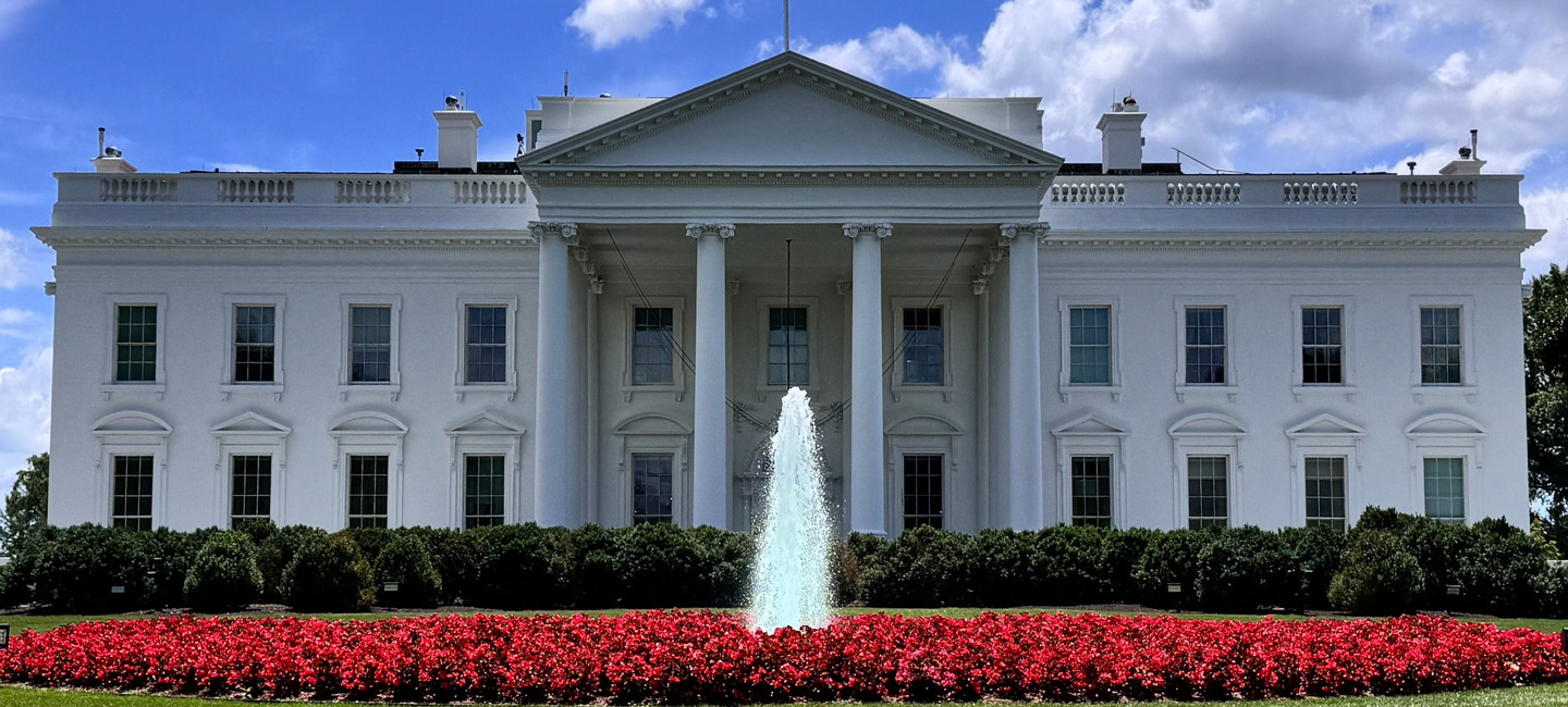 Blick auf das Weiße Haus in Washington an einem sonnigen Tag. Vor dem Weißen Haus sprudelt eine kleine Fontäne aus einem Brunnen.