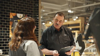 Ein Lebensmittelfachverkäufer und eine Kundin stehen am Tresen in einem Supermarkt