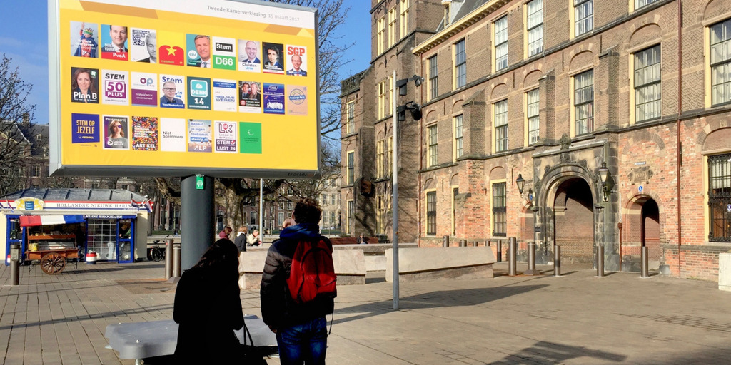 A woman and a man are standing in front of the entrance to the Binnenhof, the Dutch parliament in The Hague, and are looking at some election posters for the Dutch parliamentary election of 2017.