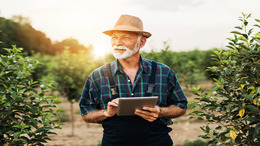 [Translate to English:] Ein Landwirt steht in einem Feld und hält ein Tablet in der Hand