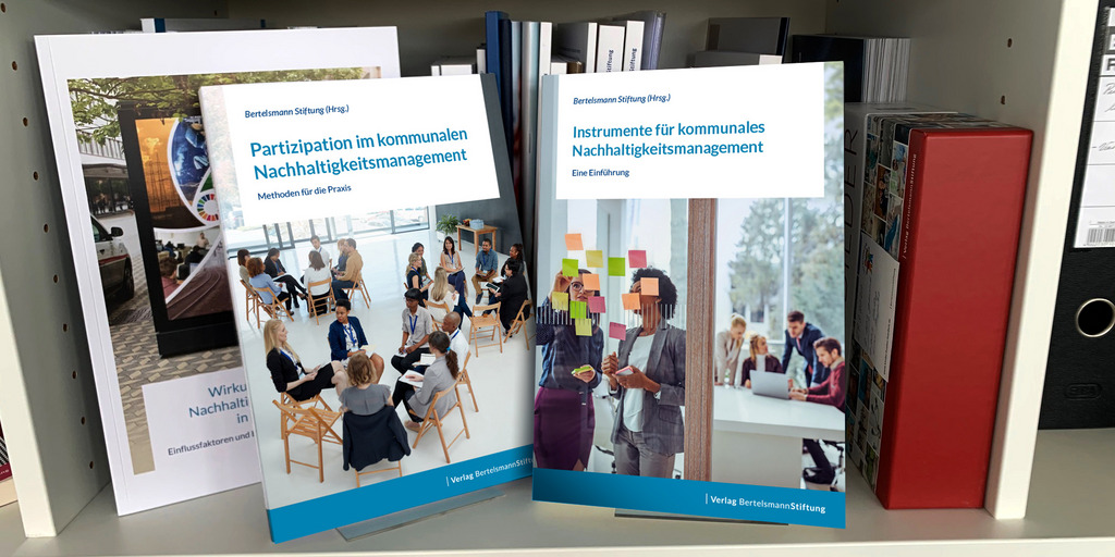 Beide Publikationen stehen auf Bücherstehlen in einem weißen Bücherregal