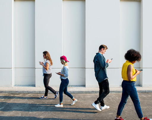 Junge Erwachsene, die beim Gehen im Freien Smartphones benutzen.  