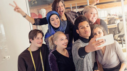 A group of non-Muslim and Muslim young people take a selfie in an office, smiling for the camera of the smartphone.