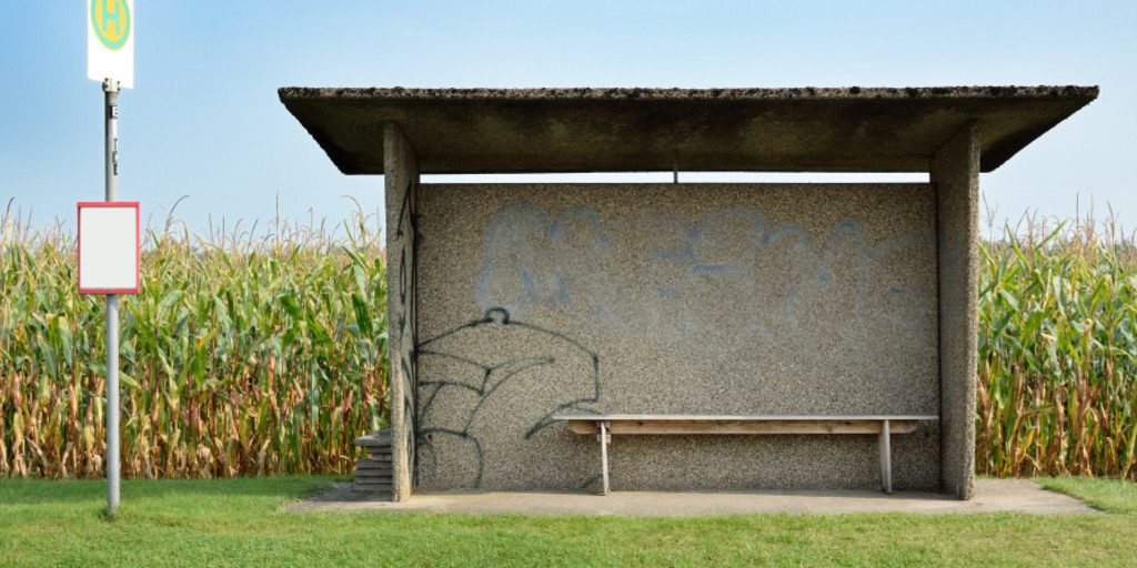 Eine verlassene Bushaltestelle auf dem Land, hinter ihr befindet sich ein Maisfeld.