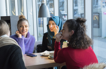 Vier junge Frauen, darunter eine mit Kopftuch, unterhalten sich in einem Café an der Oranienburger Straße in Berlin-Mitte.
