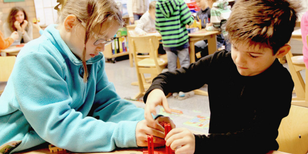Ein Mädchen und ein Junge spielen in einem Klassenzimmer einer inklusiven Schule an einem Tisch.