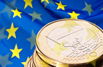 Ein Stapel Ein-Euro-Münzen ist vor einer Europaflagge zu sehen.