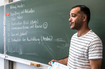 Ein Lehrer mit Migrationshintergrund steht vor der Tafel und unterrichtet seine Klasse.