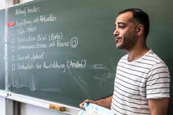 Ein Lehrer mit Migrationshintergrund steht vor der Tafel und unterrichtet seine Klasse.