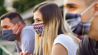 Drei Menschen mit Maske blicken in eine Richtung