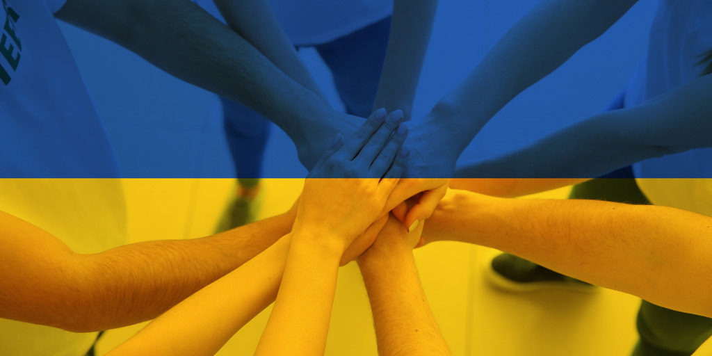 übereinanderliegende Hände vor dem Hintergrund einer Ukraineflagge