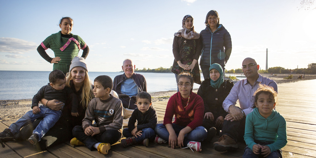 eine Gruppe von geflüchteten Menschen sitzt auf einem Steg am Ufer eines Sees
