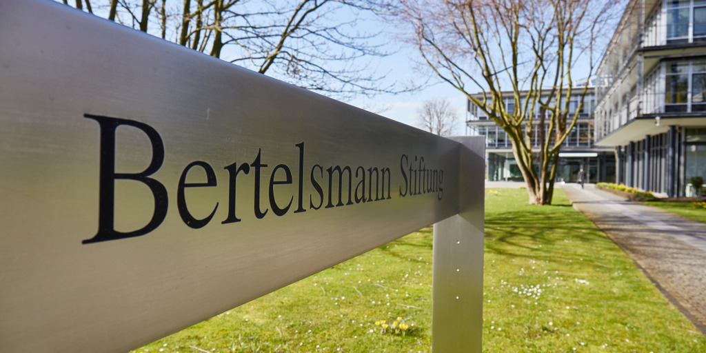 Aufnahme des Schildes mit der Aufschrift "Bertelsmann Stiftung" am Haupteingang zum Stiftungsgebäude, der Haupteingang ist im Hintergrund zu sehen