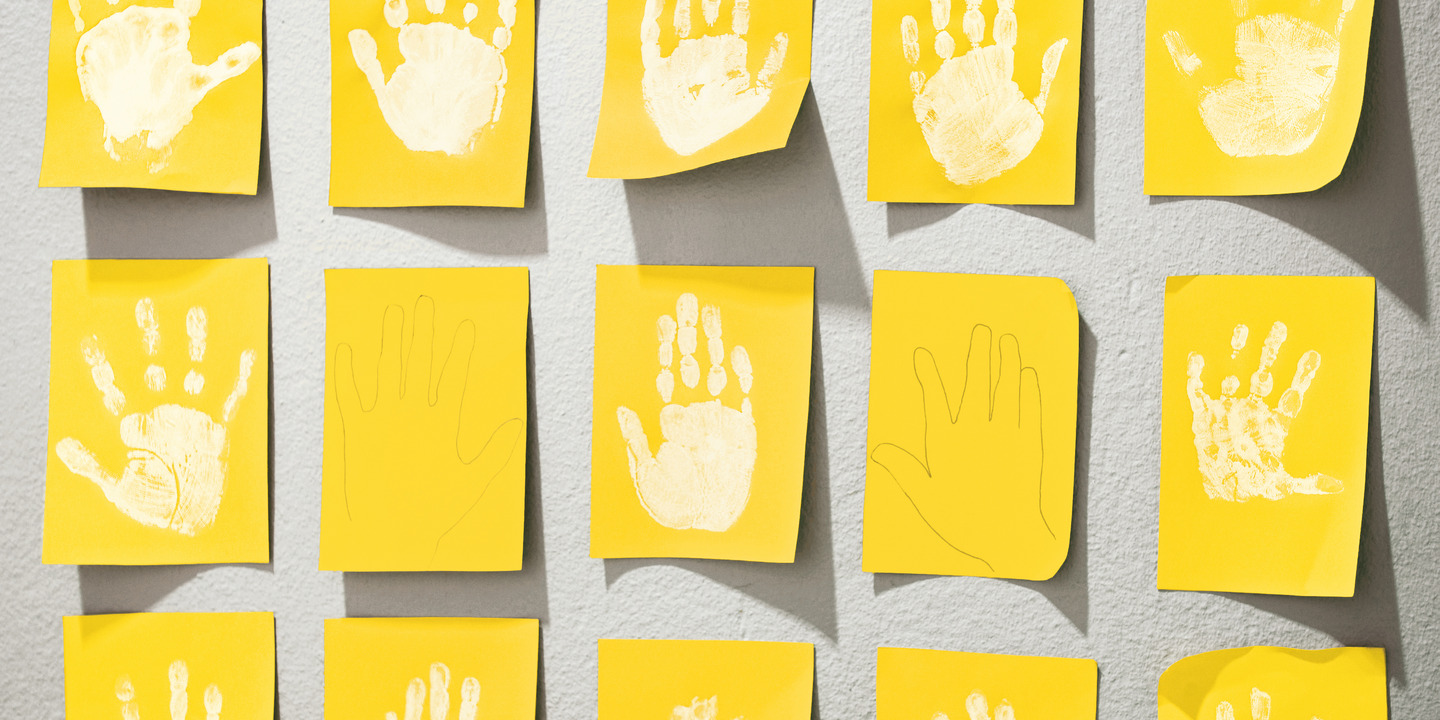 Weißfarbige Abdrücke von Kinderhänden auf gelben Pappkarten hängen an einer Wand