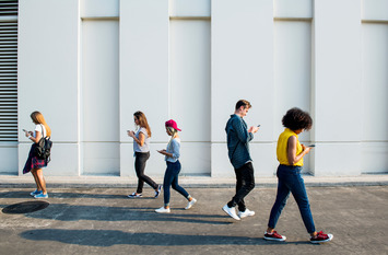 Mehrere junge Menschen gehen durch eine Stadt und blicken dabei auf ihre Smartphones.