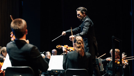 Cornelius Meister steht am Dirigentenpult und dirigiert das Orchester.