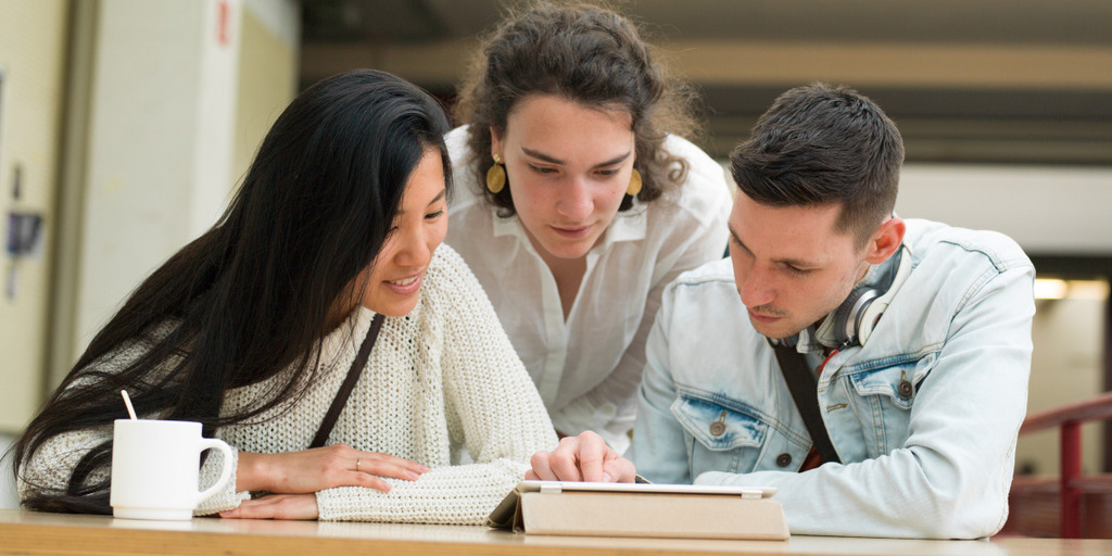 Three young people are looking to an iPad.