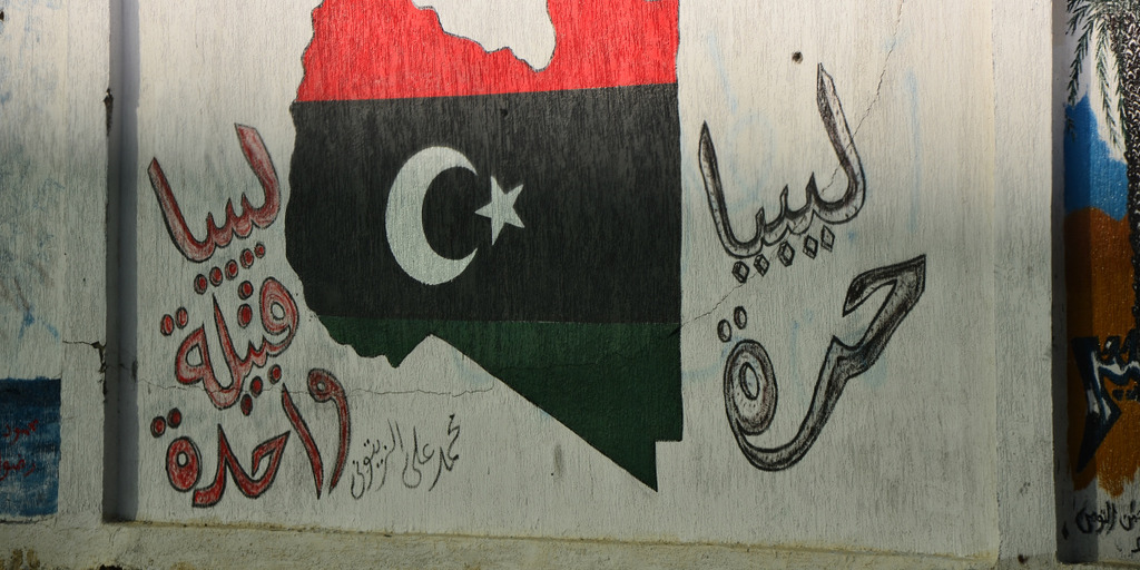 Malerei auf einer weißen Hauswand. Zu sehen sind die libysche Nationalflagge, die die Form der Landesgrenzen hat.