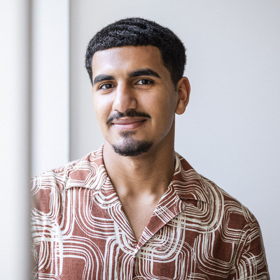 2024_Praesenztreffen_JugendCommunity Junger Mann mit schwarzen kurzen Haaren grinst in die Kamera