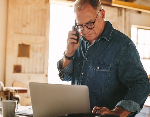 Älterer Mann bedient einen Laptop und telefoniert dabei