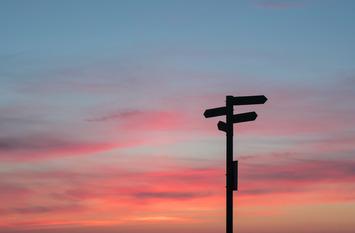 Untergehende Sonne mit einen Wegweiser im Vordergrund