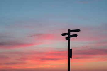 Untergehende Sonne mit einen Wegweiser im Vordergrund