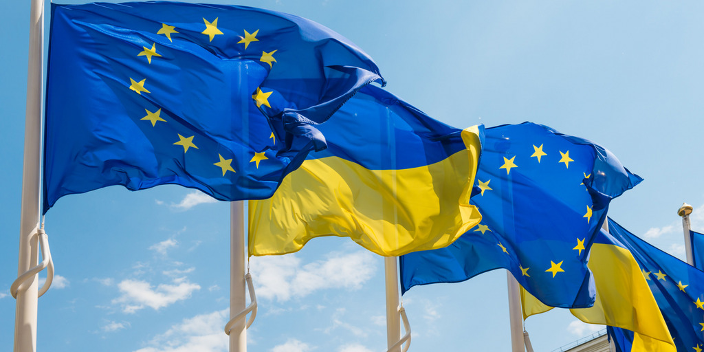 [Translate to English:] Die Flaggen der Ukraine und der Europäischen Union flattern im Wind am blauen Himmel