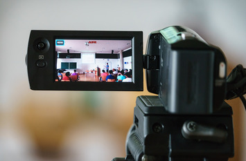 Auf dem ausgeklappten Display einer Videokamera ist eine Unterrichtssituation in einem Klassenzimmer zu sehen.
