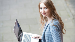 Eine junge Frau sitzt draußen auf einer Treppe mit einem Laptop auf dem Schoß
