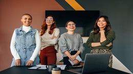Successful female entrepreneurs smiling cheerfully while standing behind a table in a boardroom. Group of multicultural businesswomen working together in a modern office